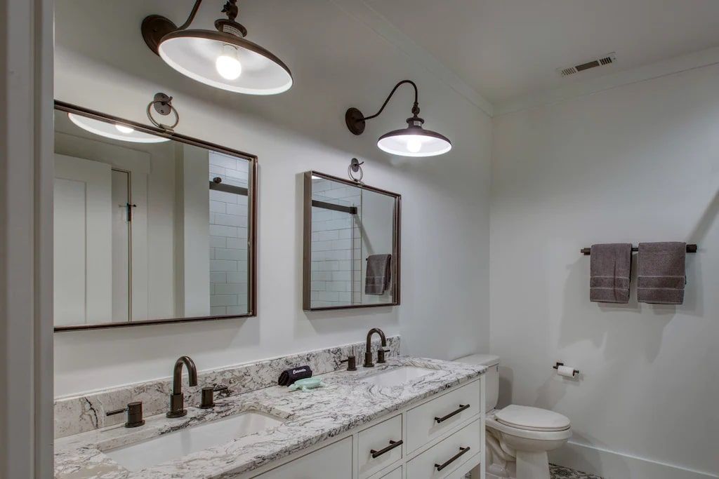 A bathroom with two sinks , two mirrors and a toilet.