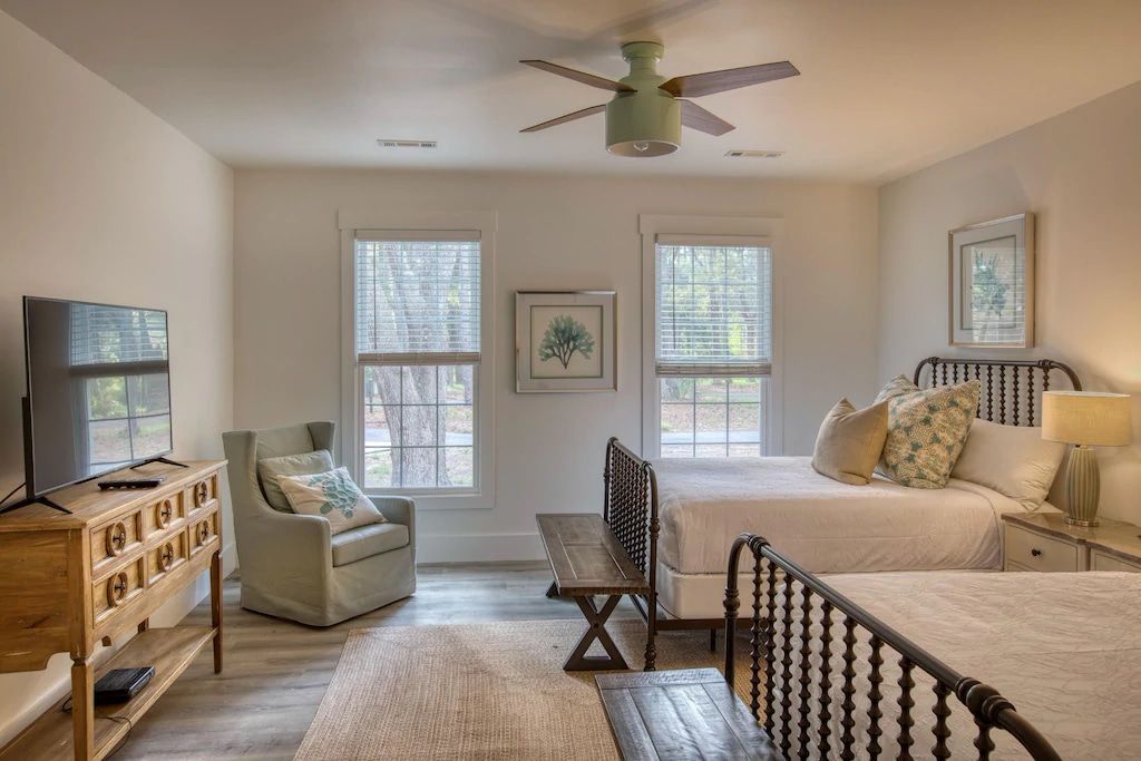 A bedroom with two beds , a chair , a television and a ceiling fan.