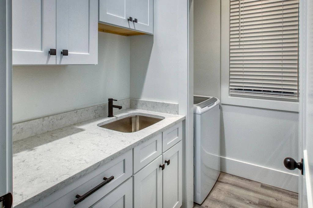 A laundry room with white cabinets , a sink , and a washer and dryer.