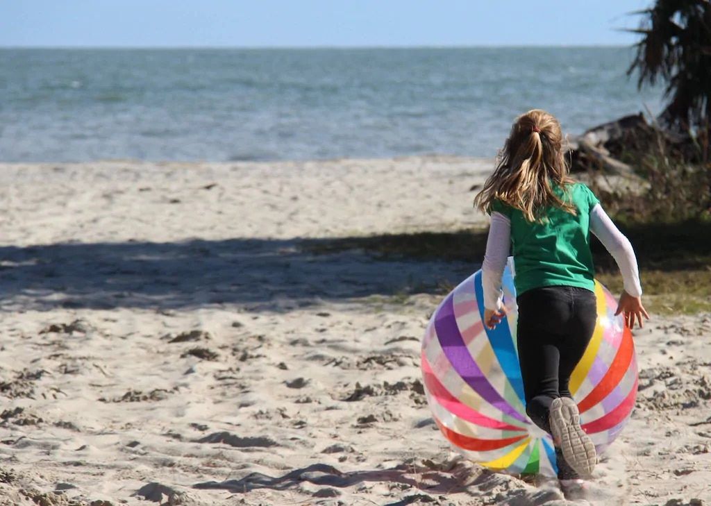 A little girl is running on the beach with a rainbow ball