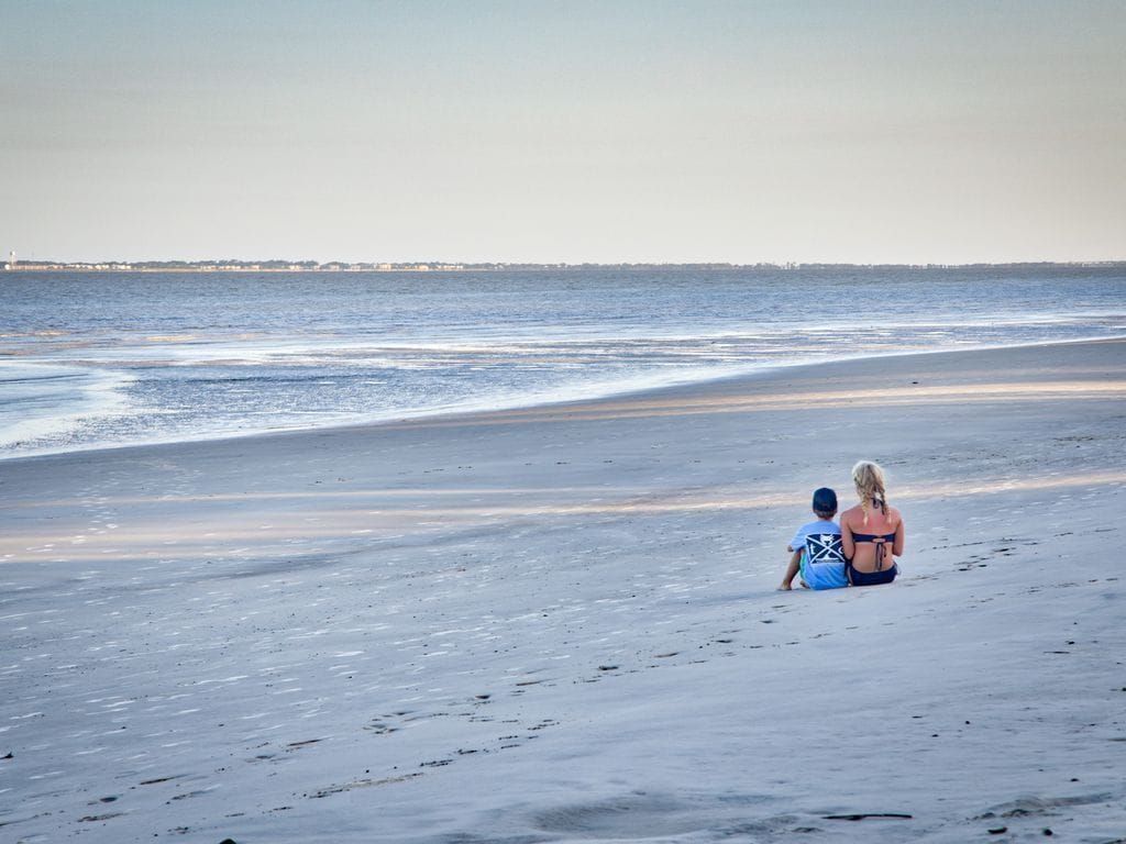 A man and a woman are sitting on the beach looking at the ocean.