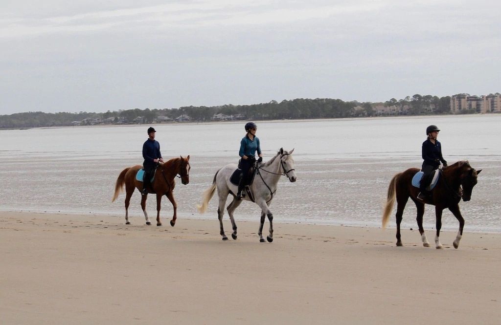 Three people are riding horses on the beach