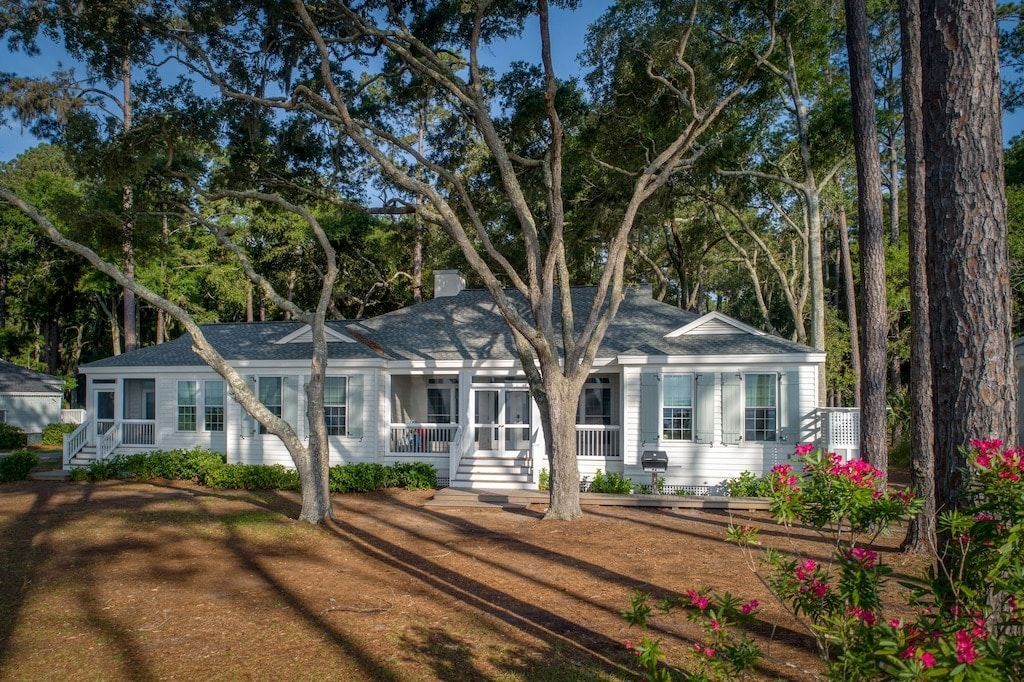 A large white house is surrounded by trees and flowers.