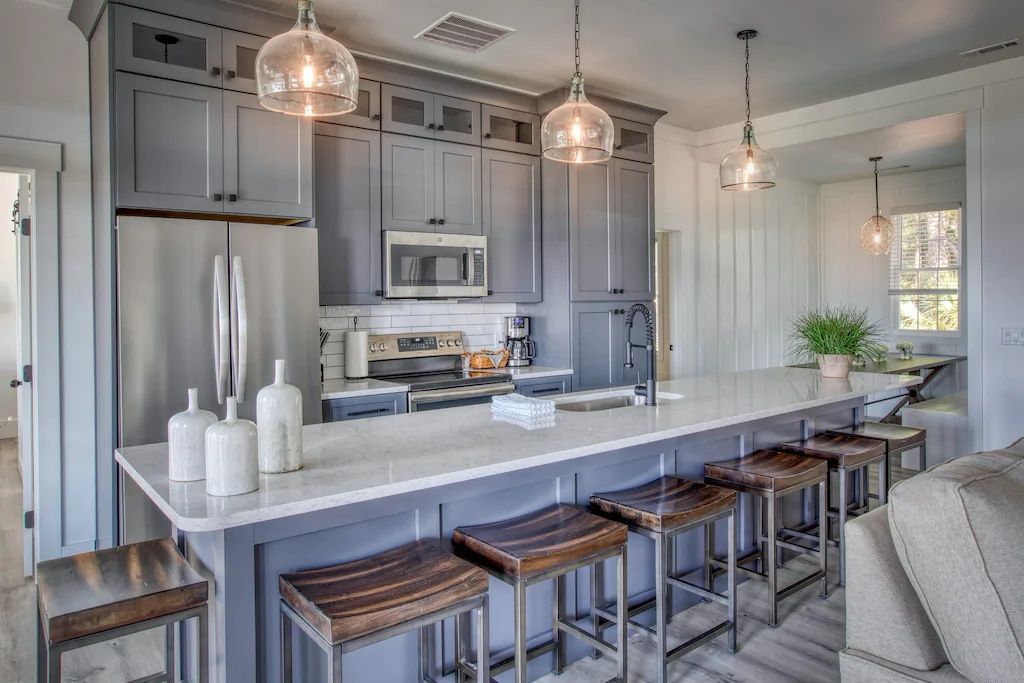 A kitchen with gray cabinets , stainless steel appliances , a large island and stools.