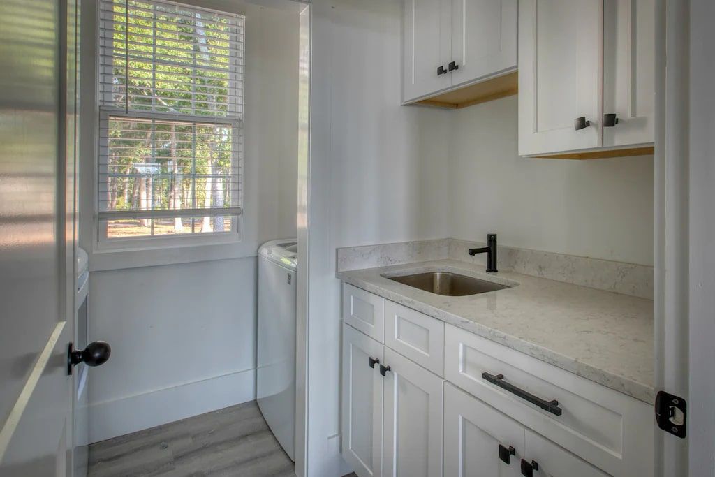 A kitchen with white cabinets , a sink , and a window.