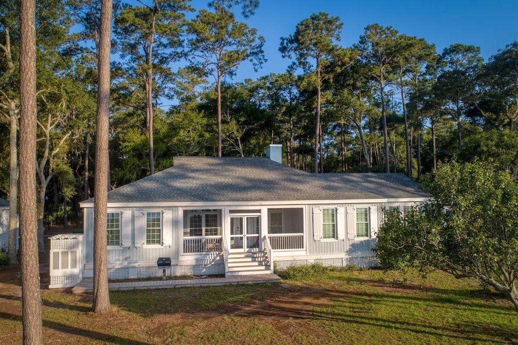 A white house with a screened in porch is surrounded by trees.
