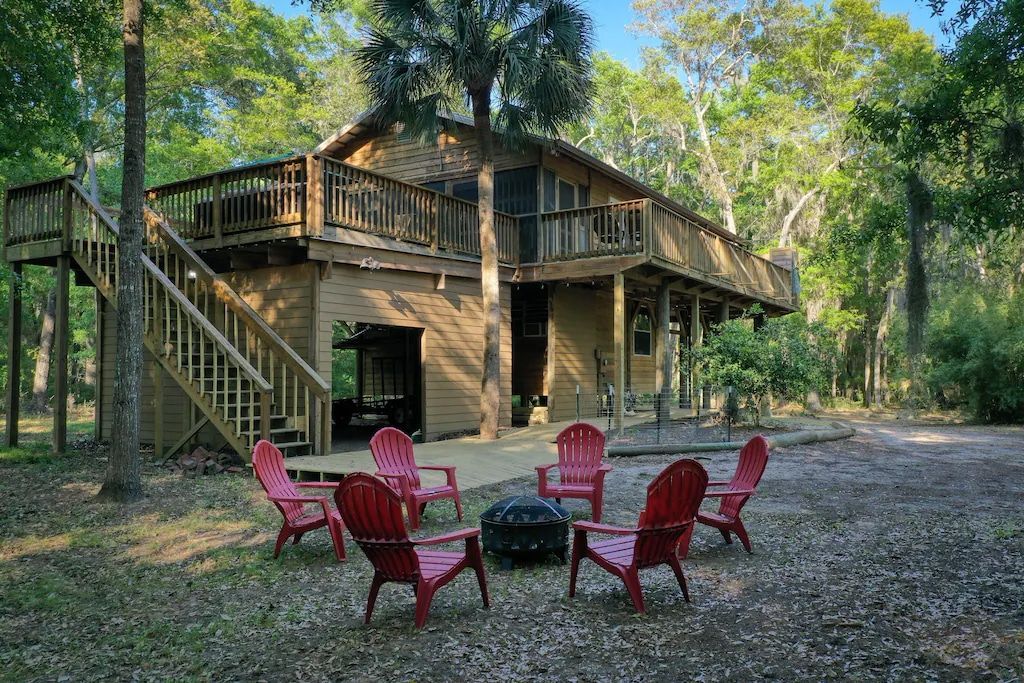 A group of red chairs are sitting around a fire pit in front of a house.