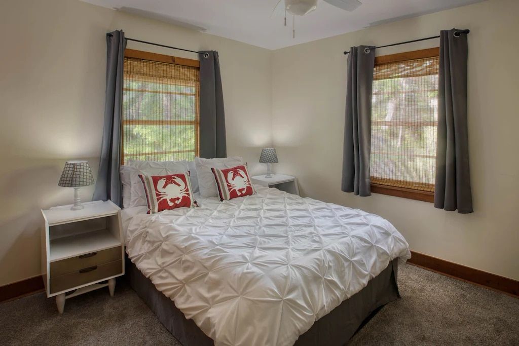 A bedroom with a bed , two nightstands , two windows and a ceiling fan.