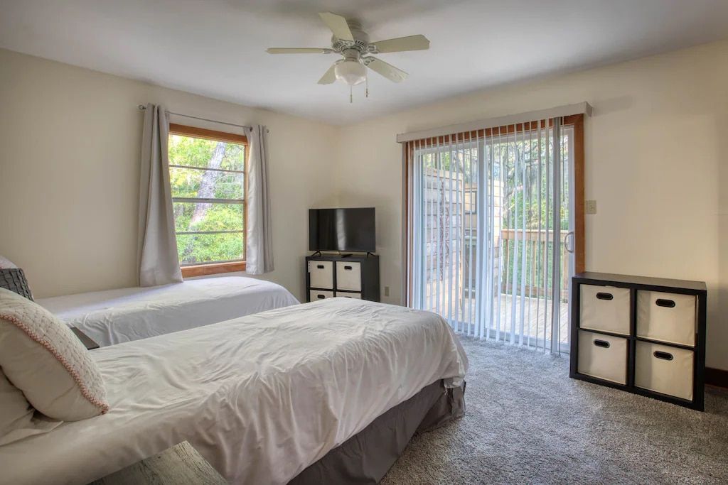 A bedroom with two beds , a ceiling fan , a television and a sliding glass door.
