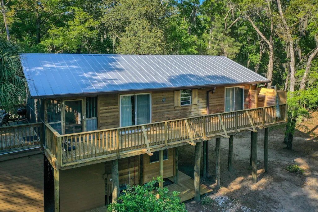 An aerial view of a wooden house with a metal roof and a large deck surrounded by trees.