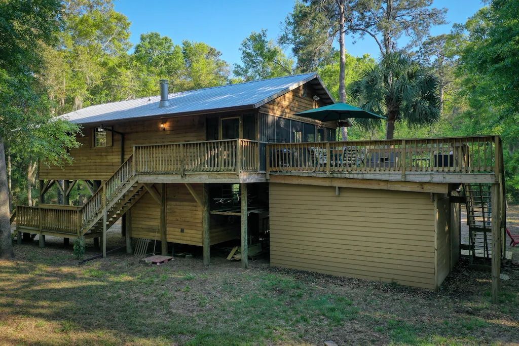 A wooden house with a large deck in the middle of a forest.