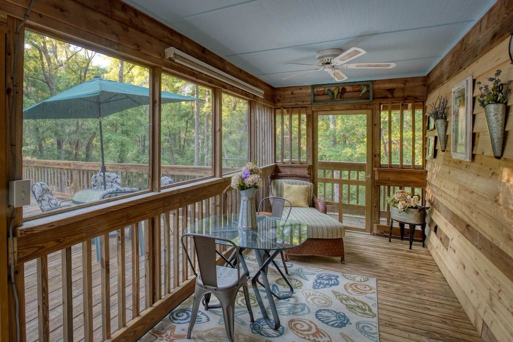 A screened in porch with a table and chairs and a ceiling fan.