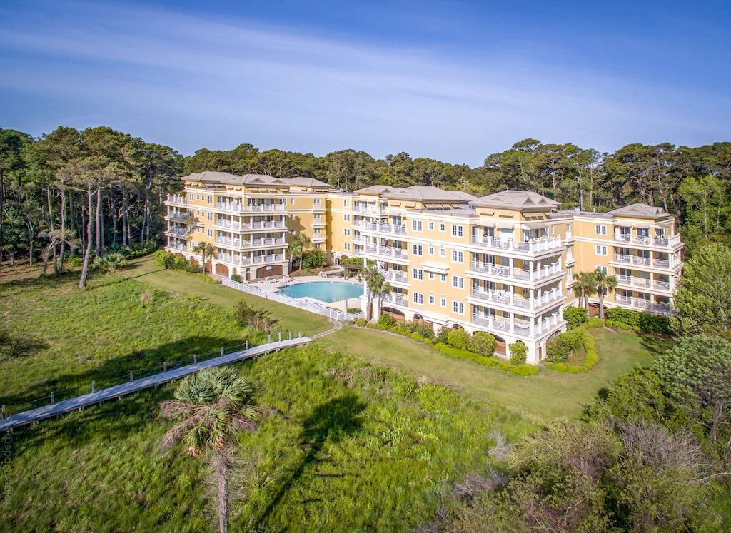 An aerial view of a large apartment building with a pool surrounded by trees.