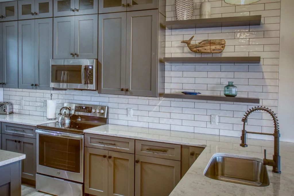 A kitchen with gray cabinets , stainless steel appliances , a sink , and a microwave.