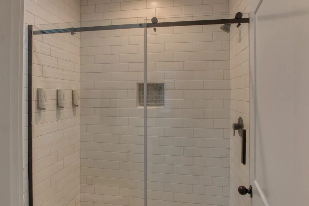 A bathroom with white tiles and a sliding glass shower door.