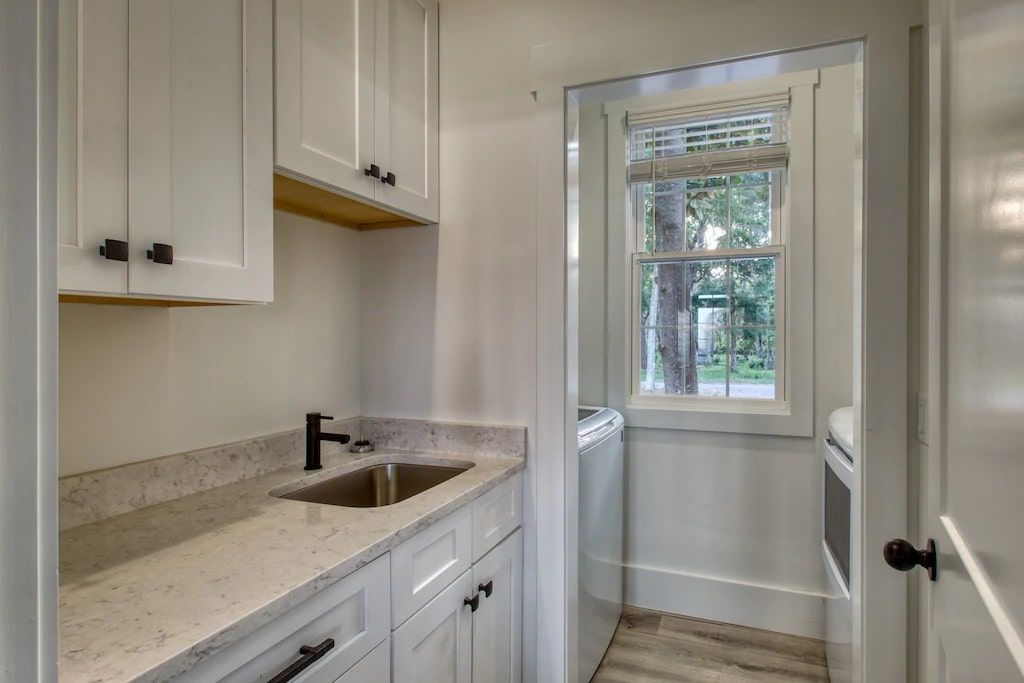 A kitchen with white cabinets , a sink , and a window.