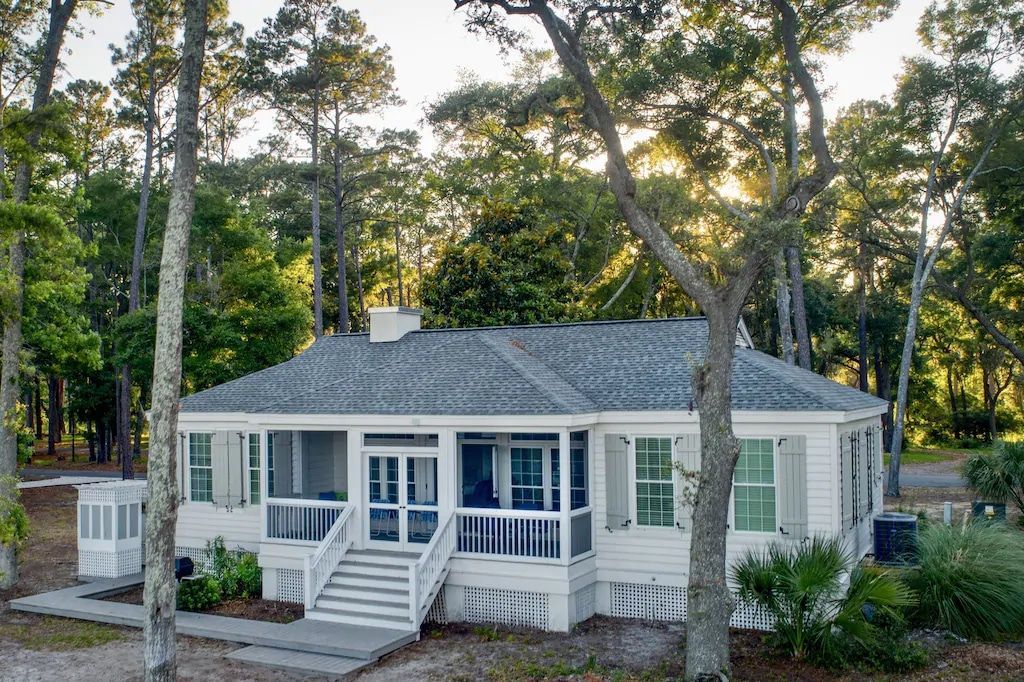 A white house with a large porch is surrounded by trees.