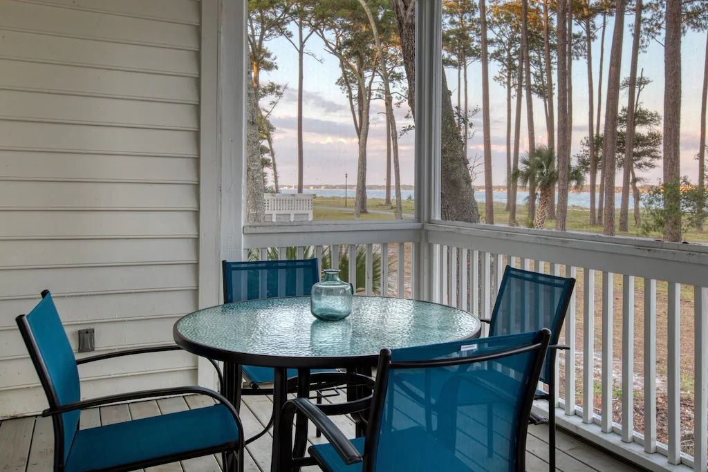 A screened in porch with a table and chairs and a view of the ocean.