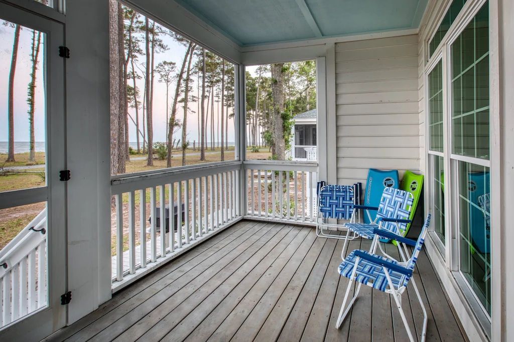 A screened in porch with chairs and a view of the ocean.