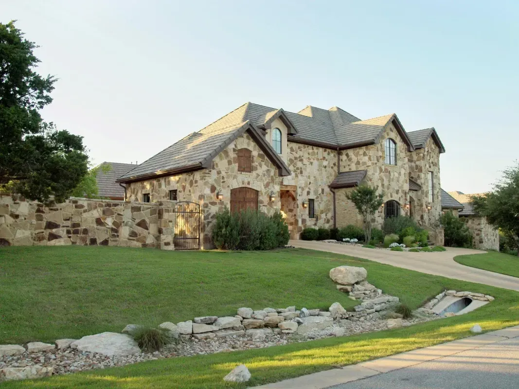 A large stone house is sitting on top of a lush green lawn.