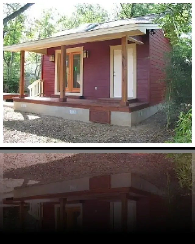 A small red house with a porch and trees in the background