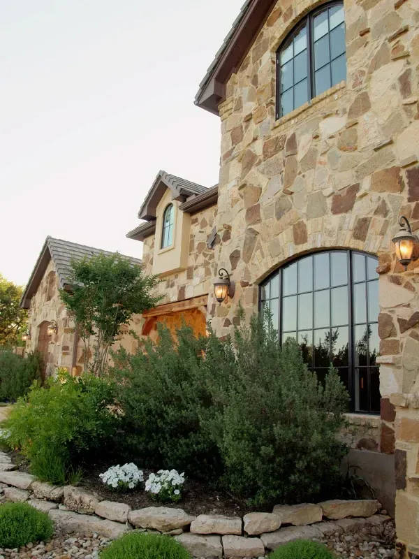 A large stone house with arched windows and bushes in front of it