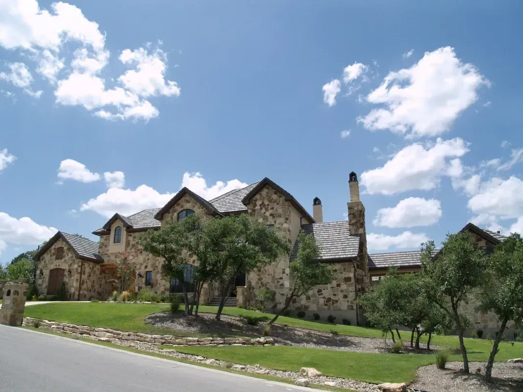A large stone house with a chimney on the roof is sitting on top of a lush green lawn.