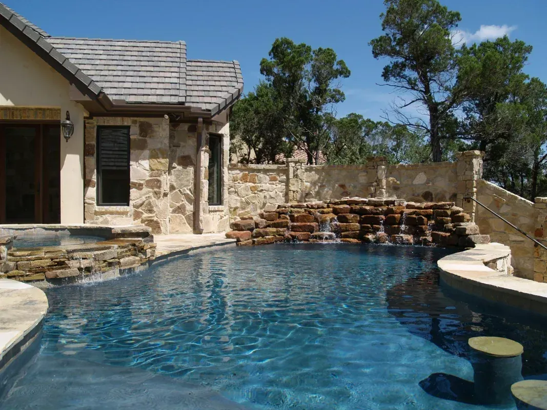 A large swimming pool with a waterfall in the backyard of a house.