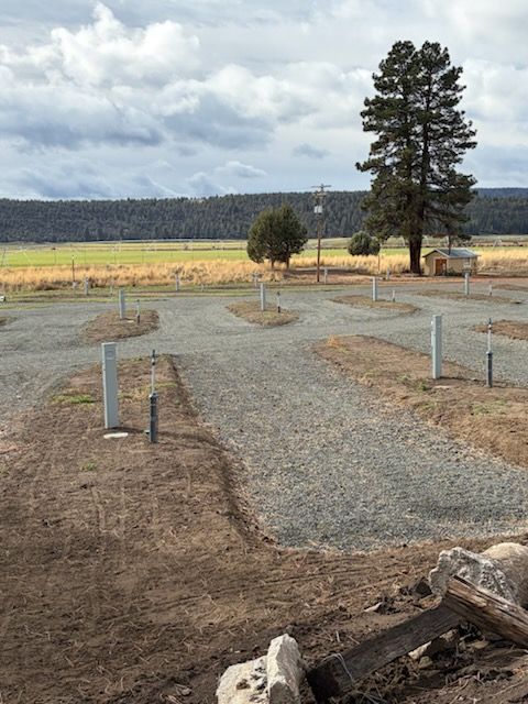 Gravel RV campsites with power and water hookups, in a grassy field with trees under a cloudy sky.