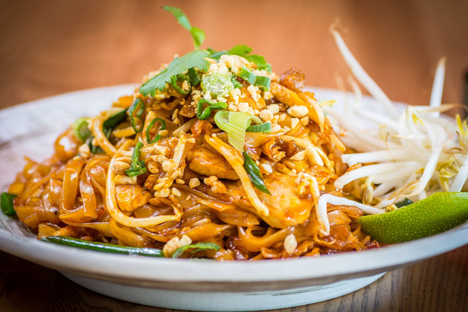 Pad Thai noodles with peanuts, bean sprouts, lime, and cilantro on a white plate.