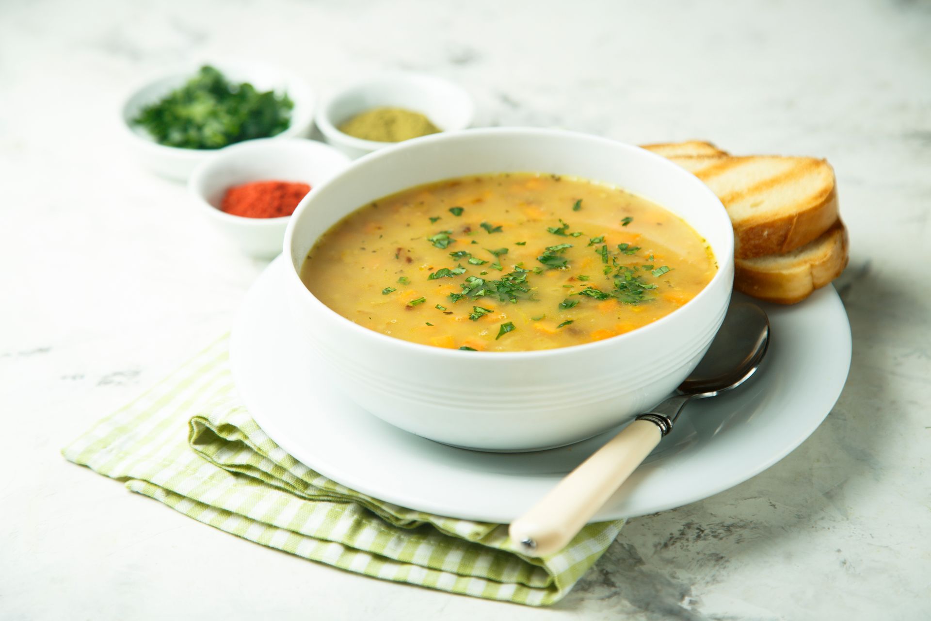 Bowl of soup garnished with parsley, with a side of toasted bread and herbs.