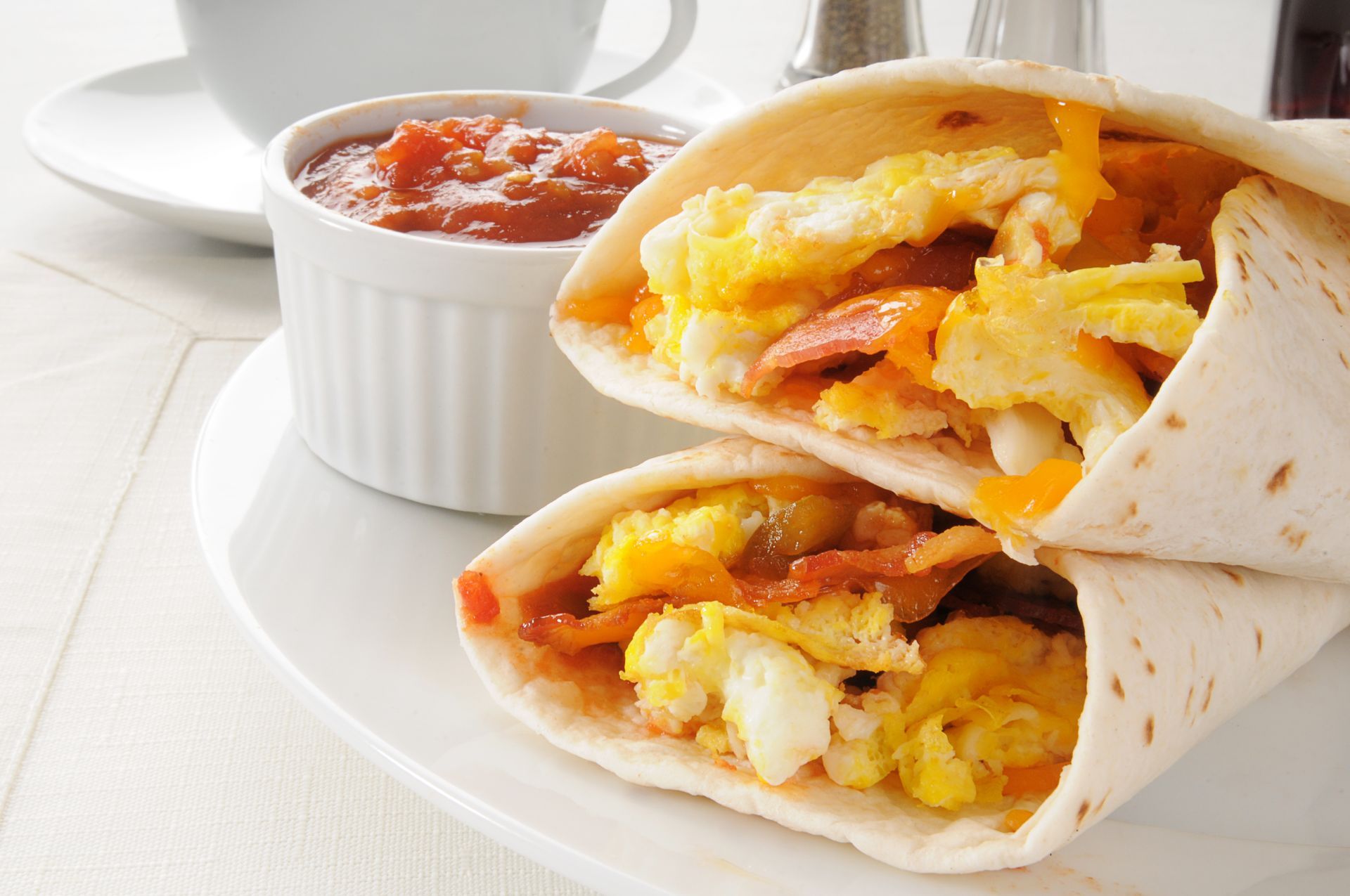 Breakfast burrito cut in half, filled with scrambled eggs, bacon, and cheese; served with salsa.