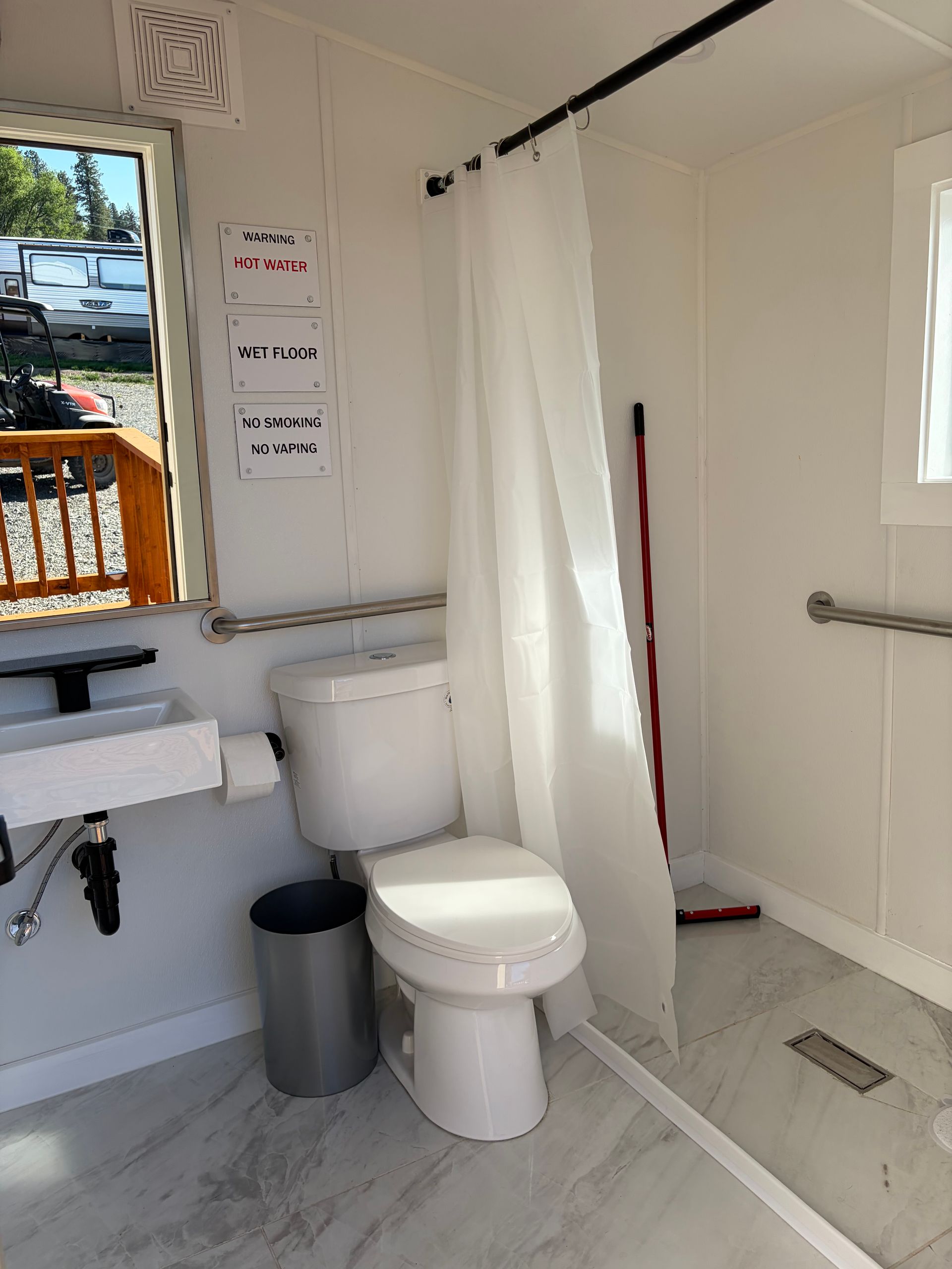 Small bathroom with toilet, sink, shower curtain, and grab bars in a white accessible stall.