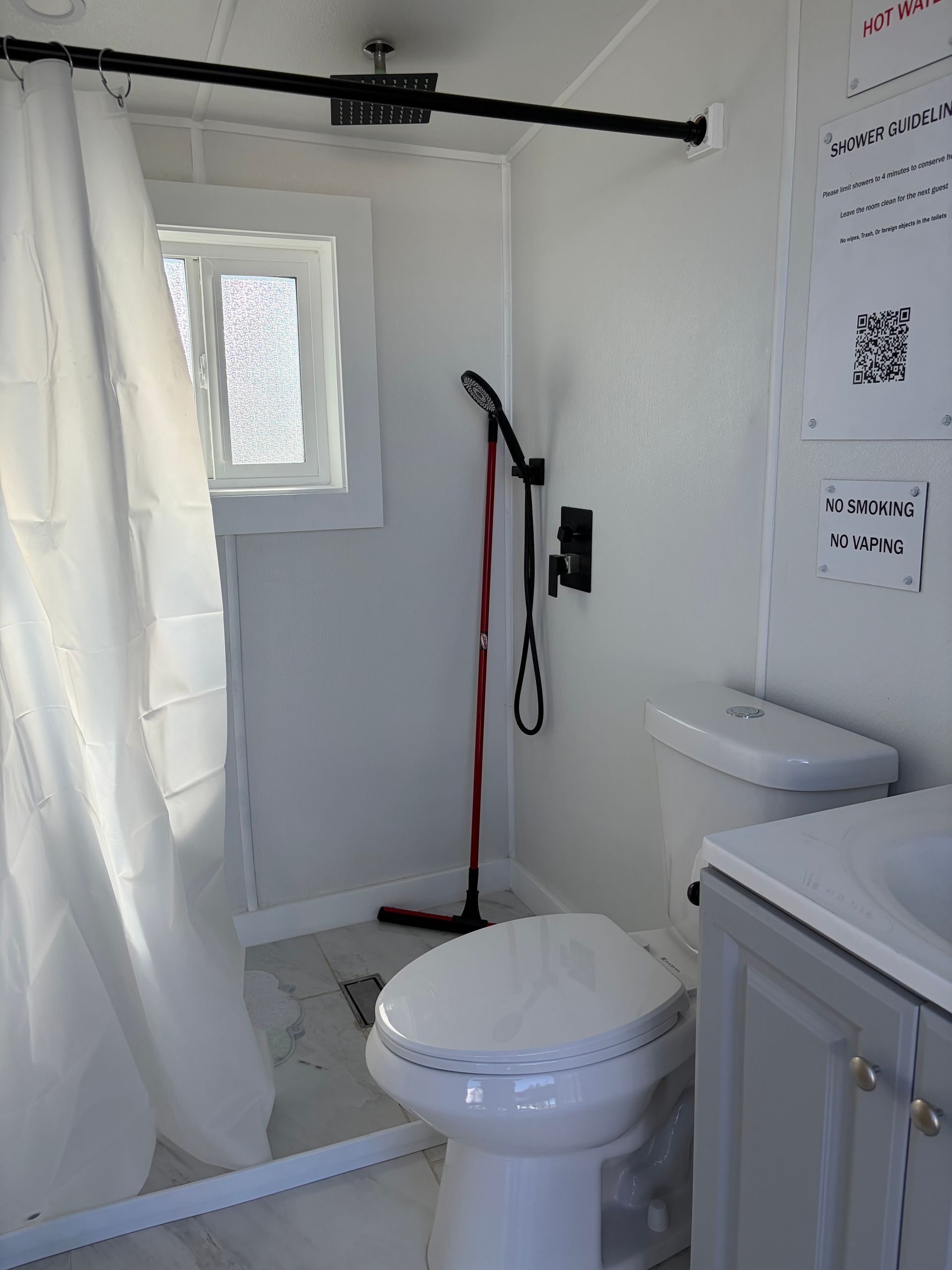 Small white bathroom with toilet, shower curtain, grab bar, and window