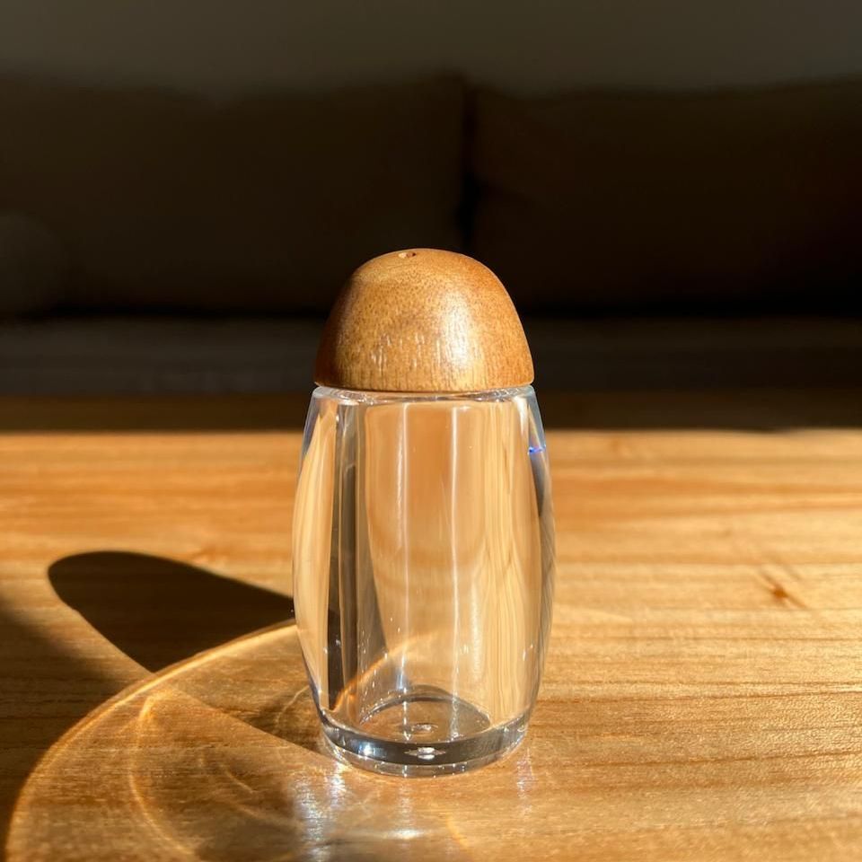 Un vaso transparente con tapa de madera está sobre una mesa de madera.