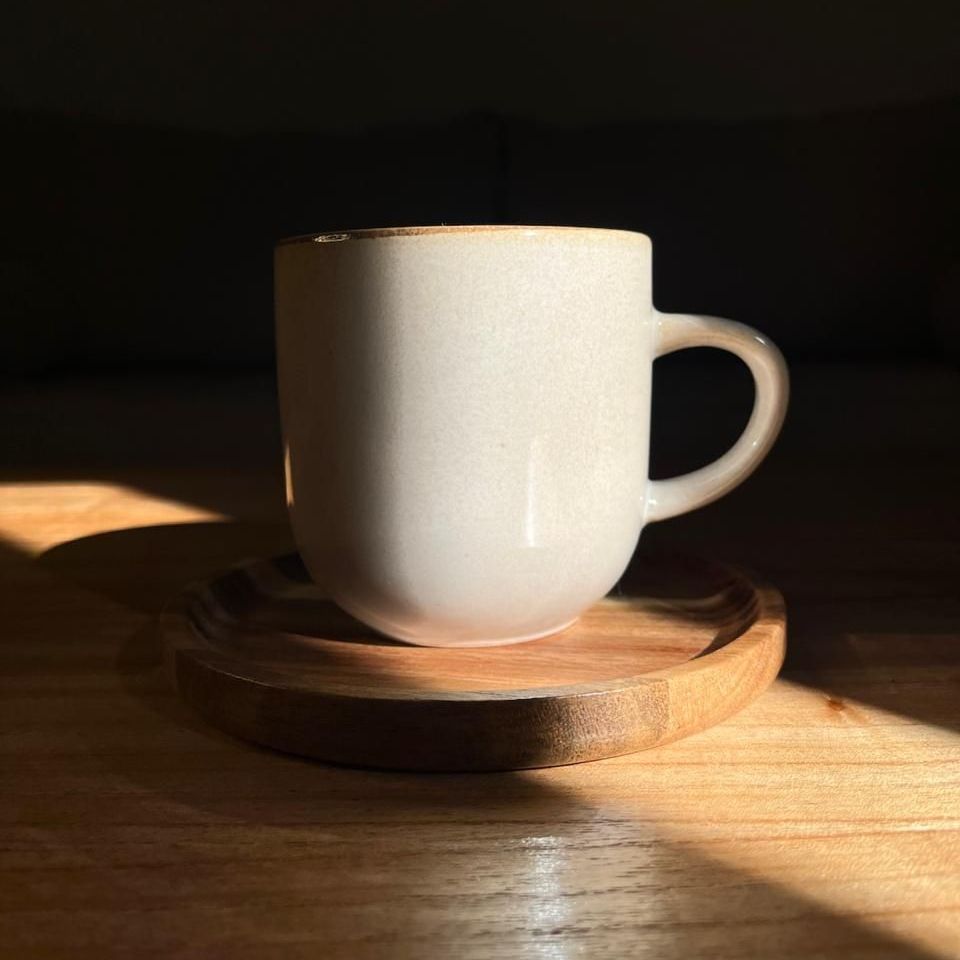 Una taza de café blanco está sobre un platillo de madera sobre una mesa de madera.