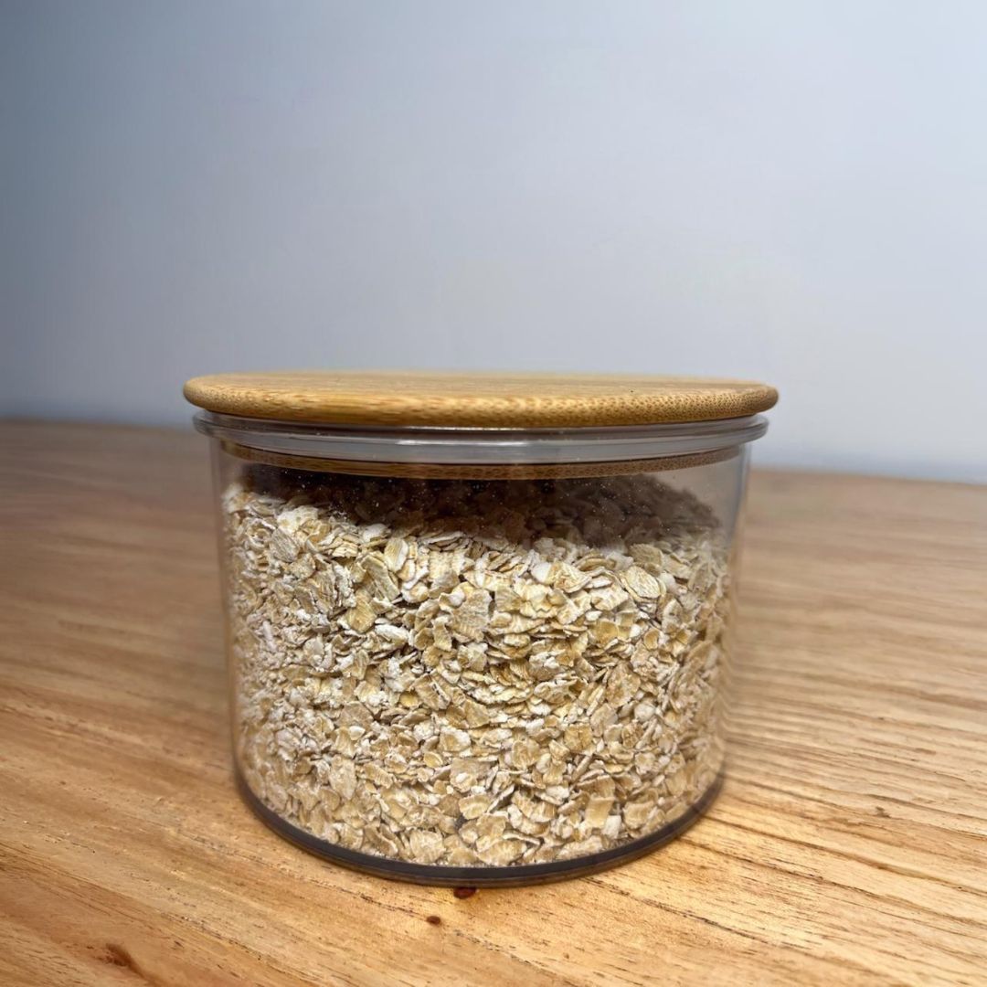 Un frasco de vidrio lleno de avena está sobre una mesa de madera.