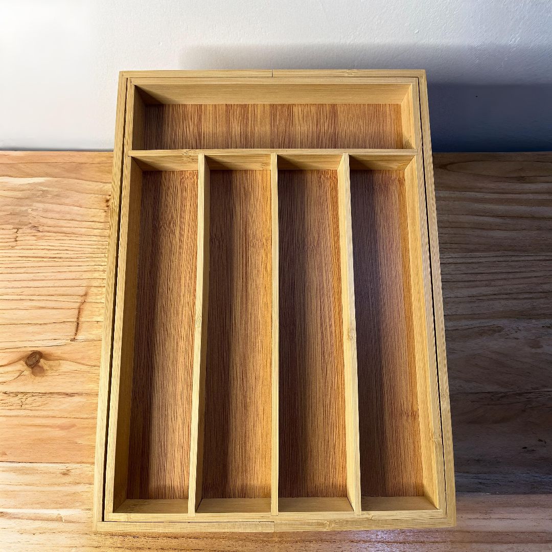 Una bandeja de cubiertos de madera está sobre una mesa de madera.