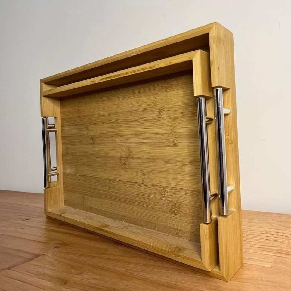 Una bandeja de madera con asas de metal está sobre una mesa de madera.