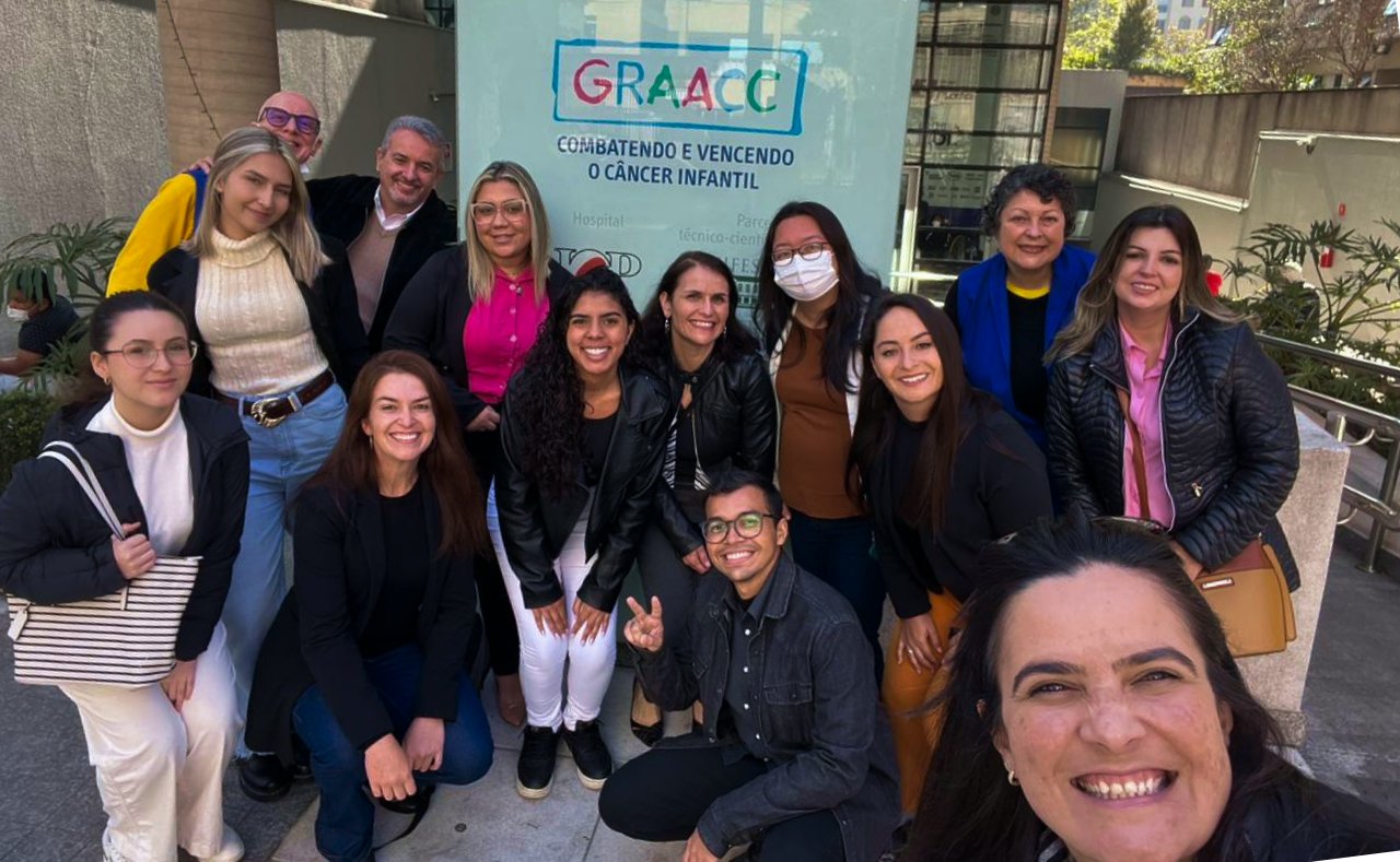 um grupo de pessoas posa para uma foto em frente a uma placa de graacc.