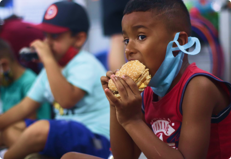 um menino usando uma máscara está comendo um hambúrguer