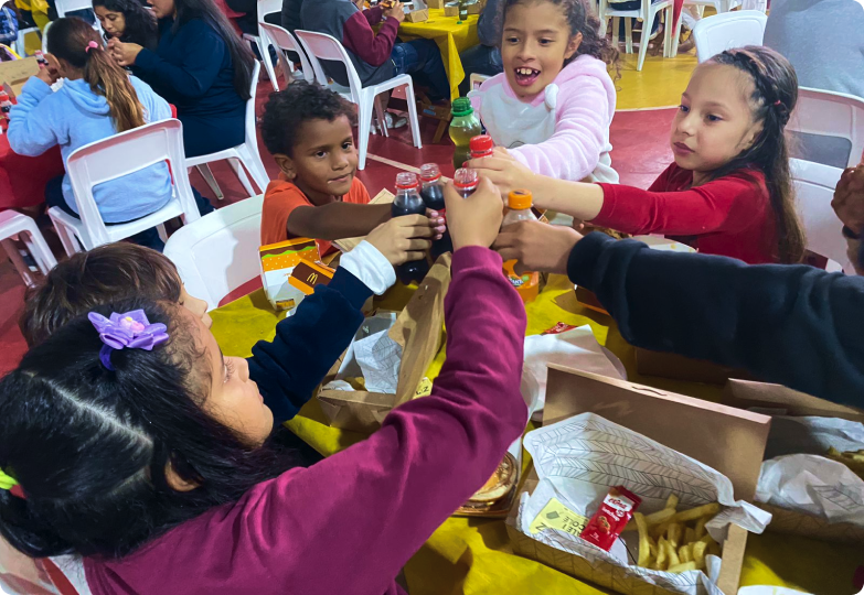 um grupo de crianças está sentado a uma mesa comendo batatas fritas e bebendo refrigerante.