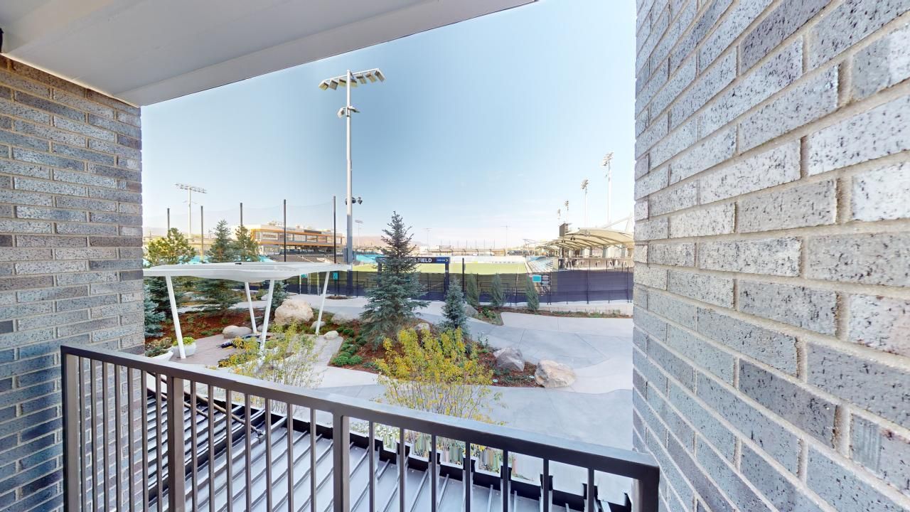 A balcony with a view of a parking lot and a brick wall.