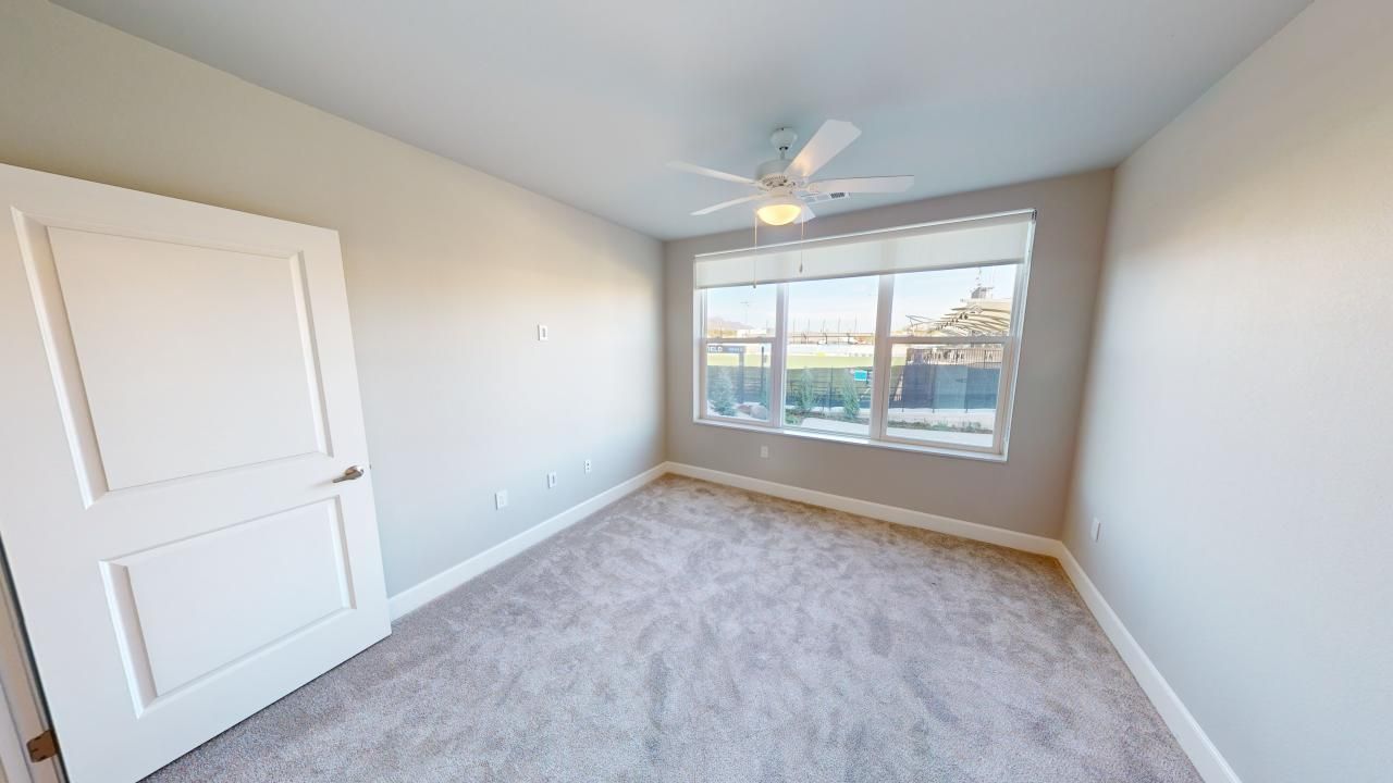 An empty bedroom with a ceiling fan and two windows.