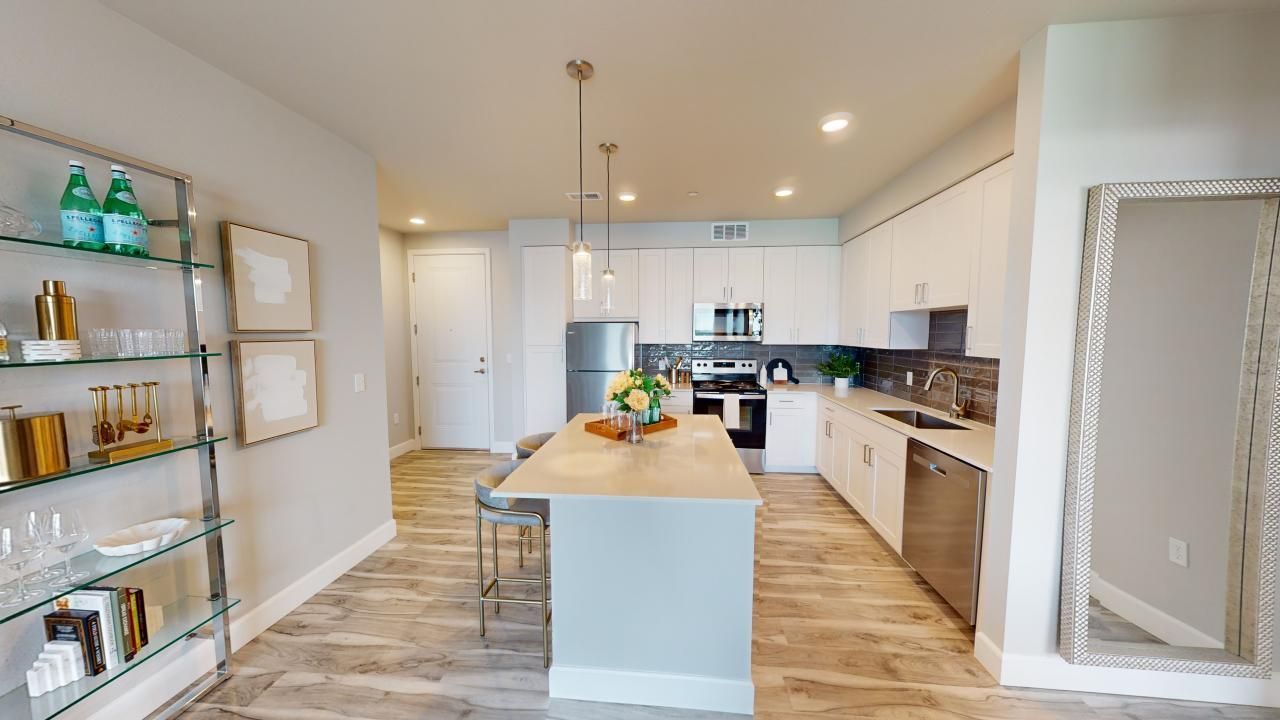 A kitchen with white cabinets, stainless steel appliances, a large island ,and a large mirror.
