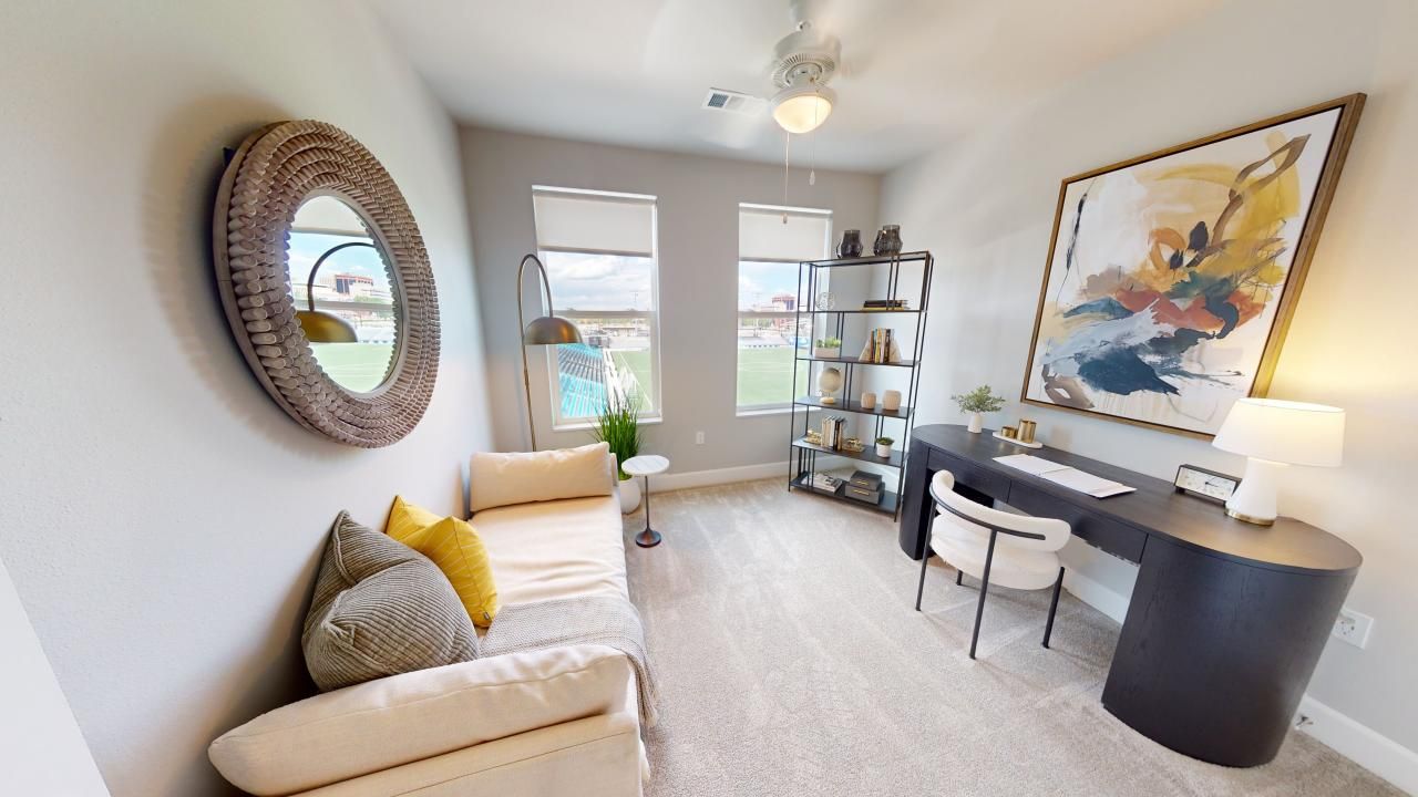 A living room with a couch, desk, chair ,and mirror.