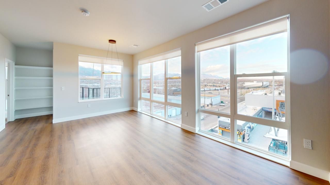 An empty living room with lots of windows and hardwood floors.