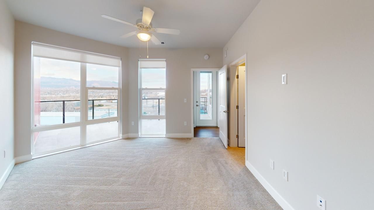 An empty living room with a ceiling fan and lots of windows.