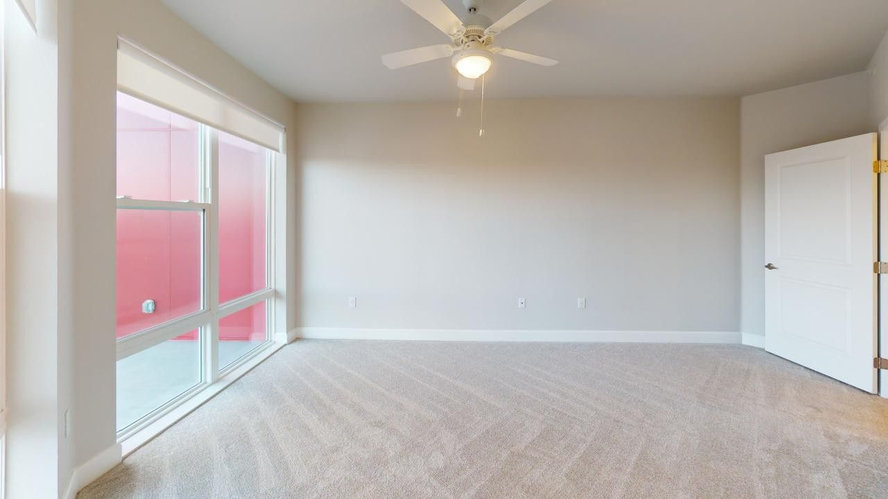 An empty room with a ceiling fan and a large window.