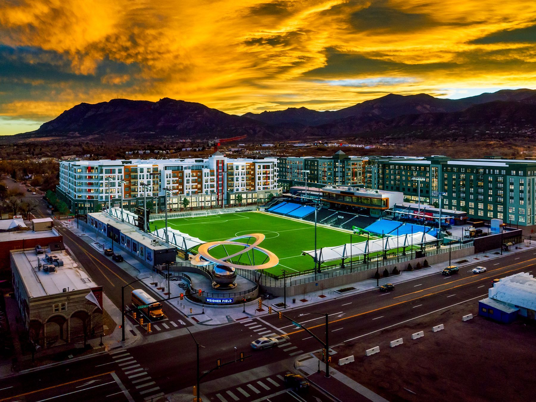 An aerial view of a baseball stadium with mountains in the background at sunset.